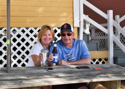 Couple on cottage picnic bench raising drinks.