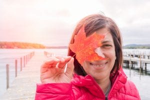 A smiling visitor holds up an amber colored leaf to showcase the New Hampshire fall foliage.